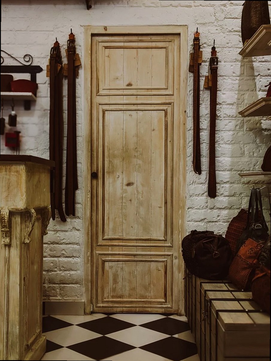 A cozy shop interior featuring leather belts and bags with a vintage wooden door.
